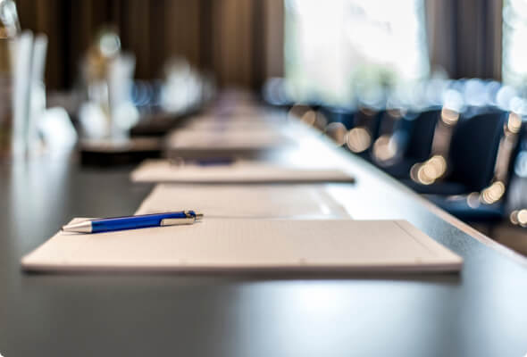 Notepads and pens lined up on a board room table 